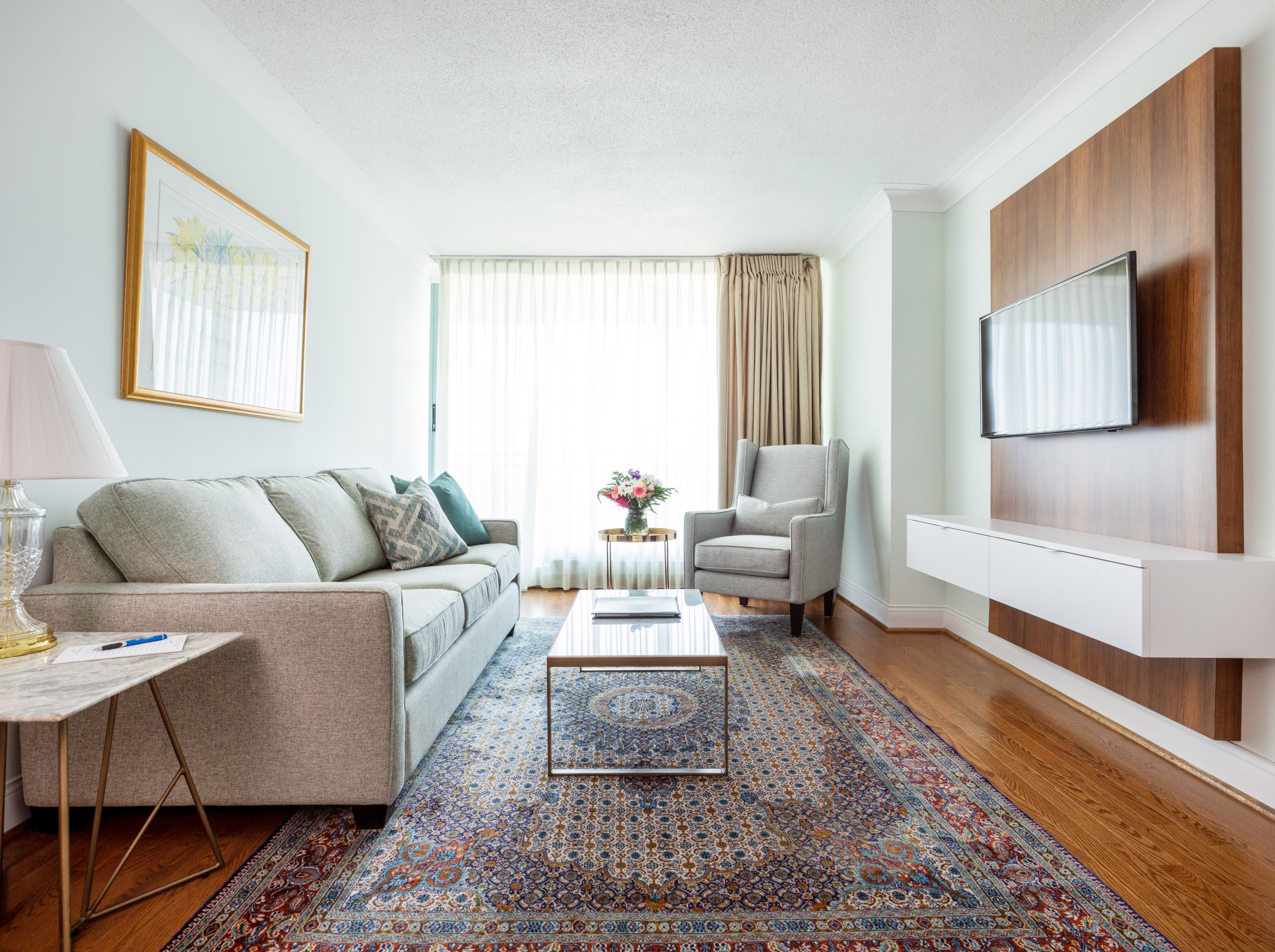 The Waterside Inn suite living room with a sofa, wood media wall and patterned rug